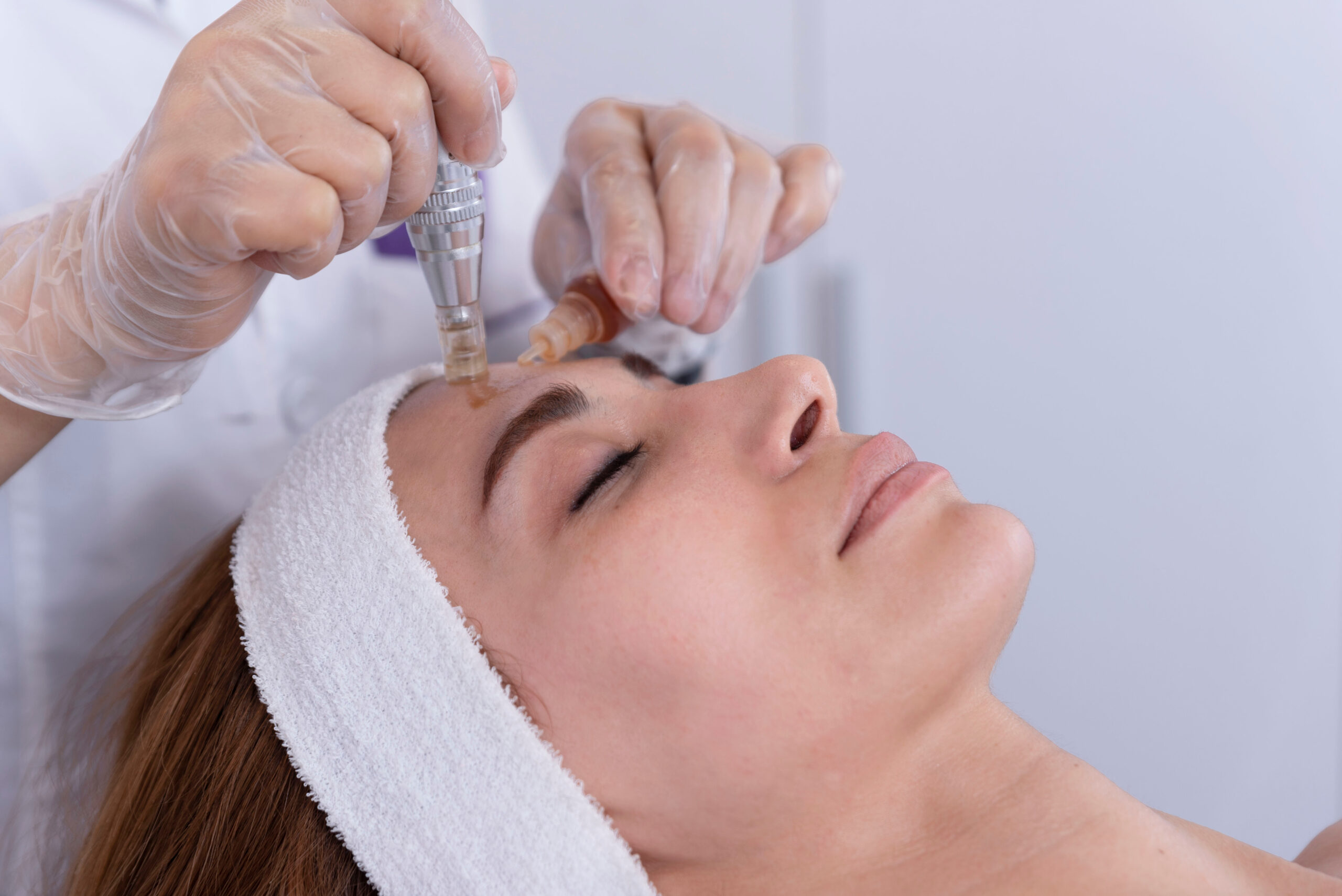 close up of Cosmetologist,beautician applying facial dermapen treatment on face of young woman customer in beauty salon.Cosmetology and professional skin care, face rejuvenation.