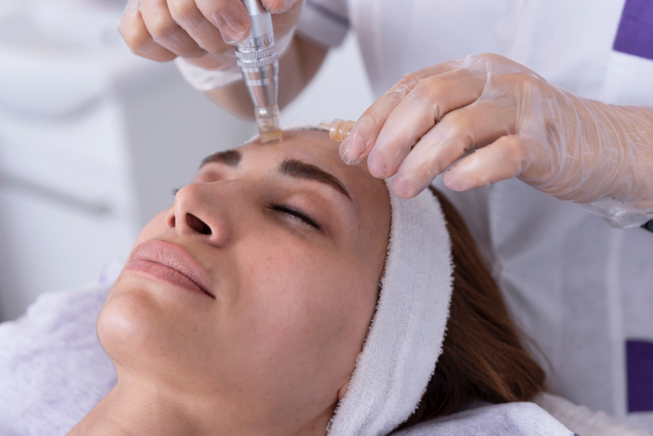 close up of Cosmetologist,beautician applying facial dermapen treatment on face of young woman customer in beauty salon.Cosmetology and professional skin care, face rejuvenation.